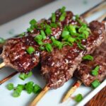 four smashed streak skewers on a plate topped with sliced green onion