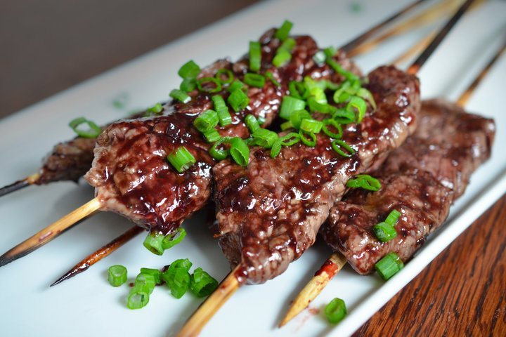 four smashed streak skewers on a plate topped with sliced green onion