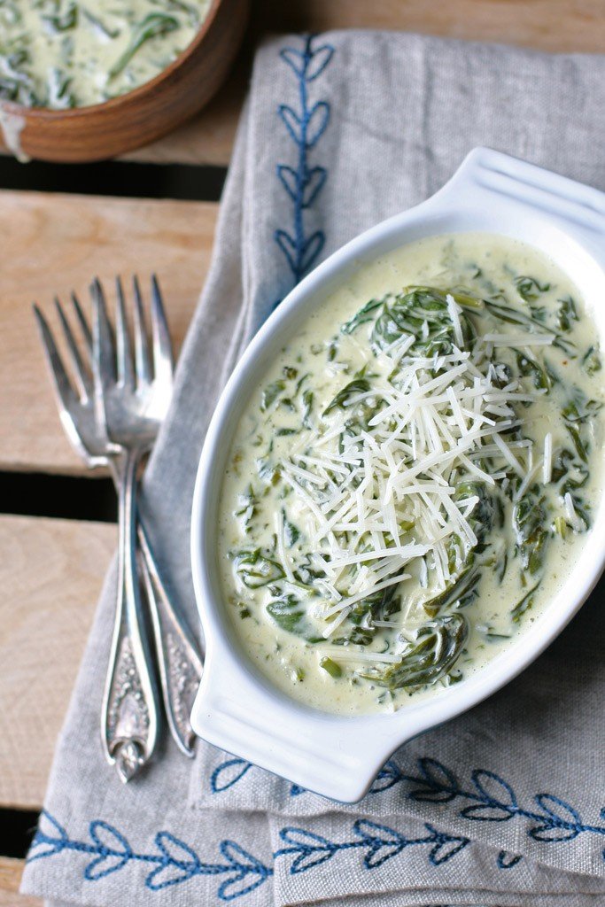 creamed spinach casserole in a casserole dish beside two forks and a towel