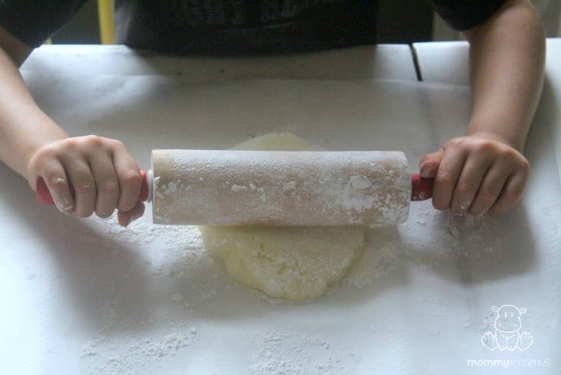 girl using rolling pin to flatten dough