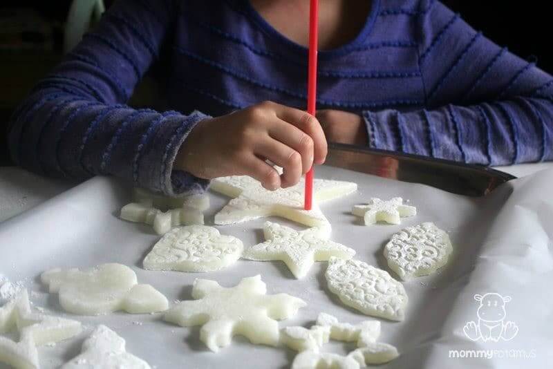 girl using a straw to poke holes in soft dough