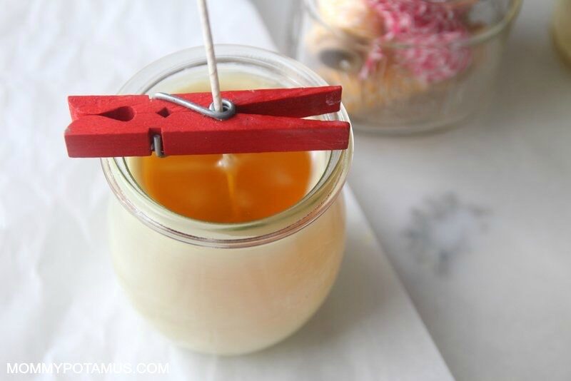 Centering candle wick upright in jar full of melted beeswax by threading it through a clothespin.