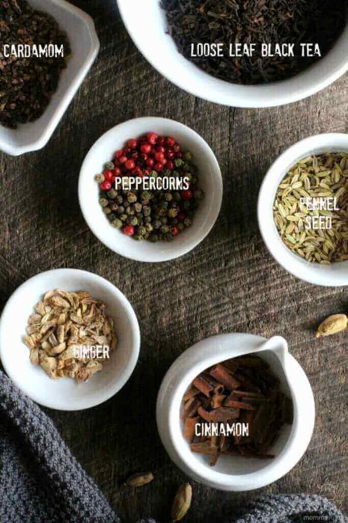 Overhead view of loose leaf black tea, whole cardamom, peppercorns, fennel seeds, dried ginger root pieces and cinnamon chips