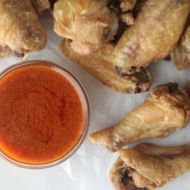 Crispy baked chicken wings on parchment paper with buffalo sauce