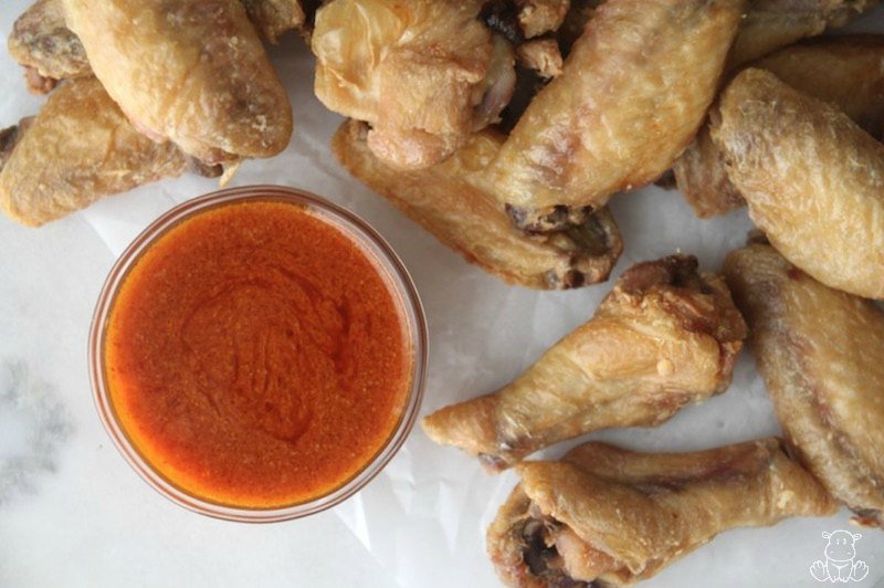 Crispy baked chicken wings on parchment paper with buffalo sauce