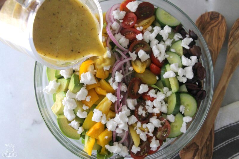 Pouring Greek salad dressing over vegetables
