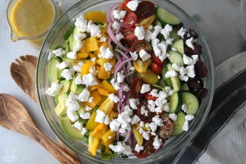 Greek salad in a bowl with dressing next to it