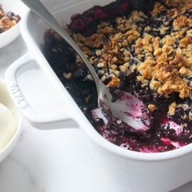 Blueberry crisp in baking dish with bowls of ice cream and crisp nearby