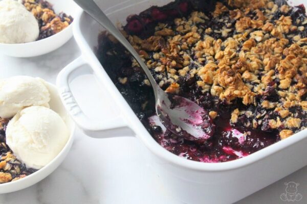 Blueberry crisp in baking dish with bowls of ice cream and crisp nearby