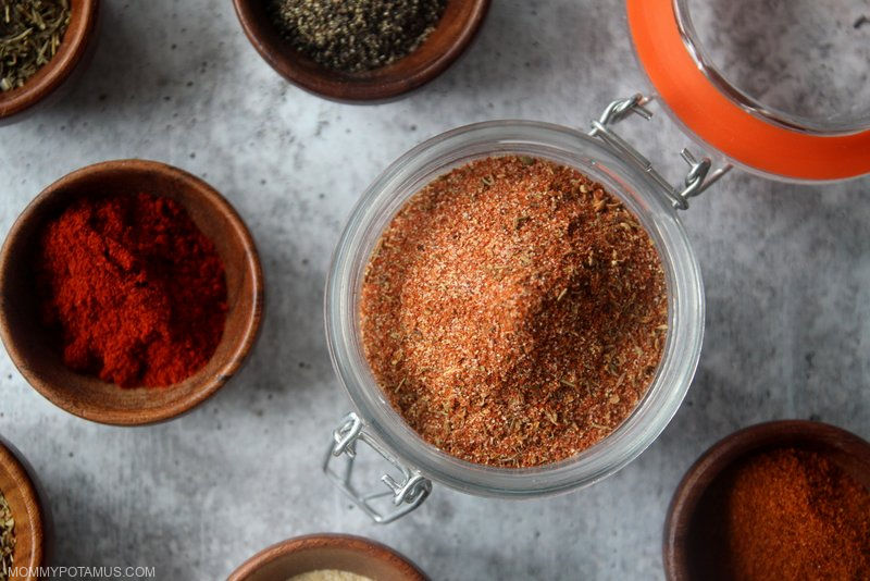 Homemade cajun seasoning in a jar surrounded by individual spices and herbs.