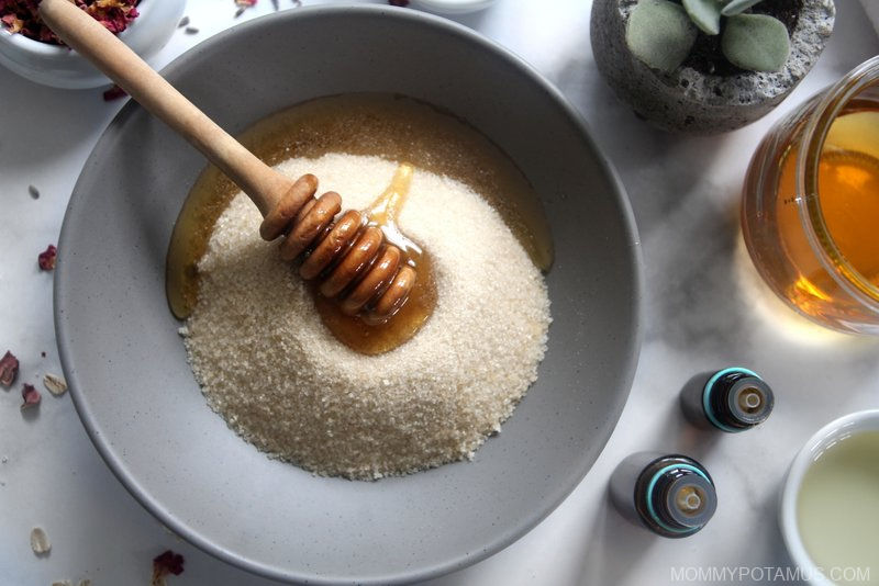 Bowl of sugar with honey dipper on top. Essential oils and oil next to bowl.