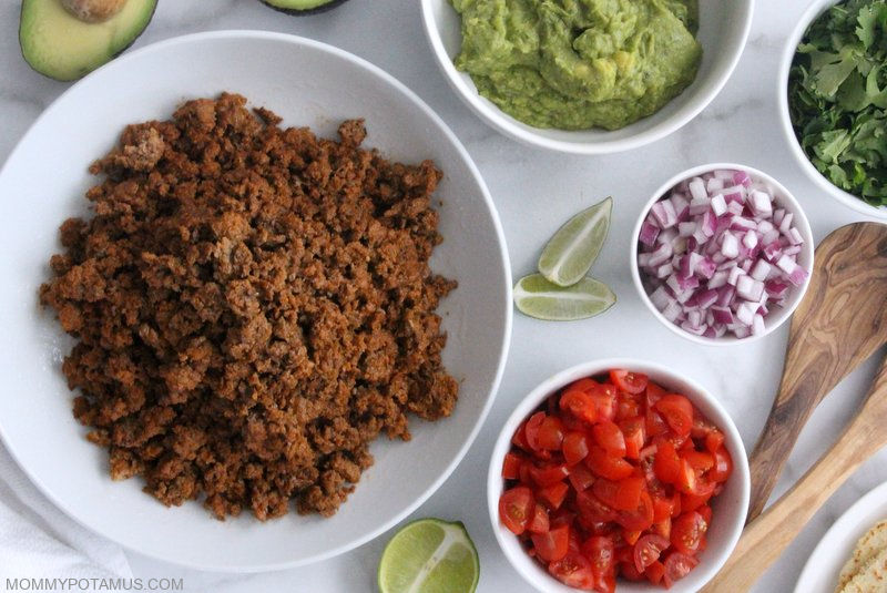 Instant pot taco meat in bowl with other bowls of sides: tomatoes, onion, guacamole and cilantro