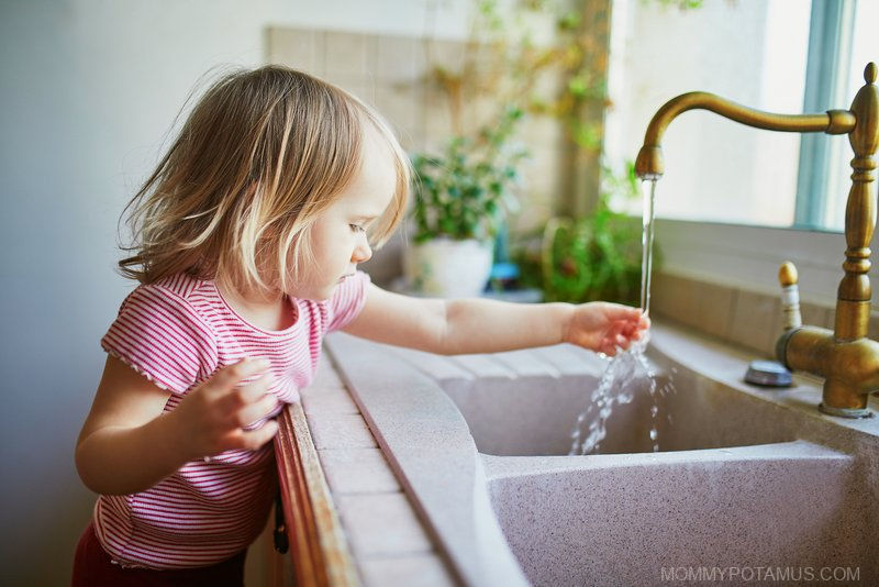 Toddler touching water pouring from faucet