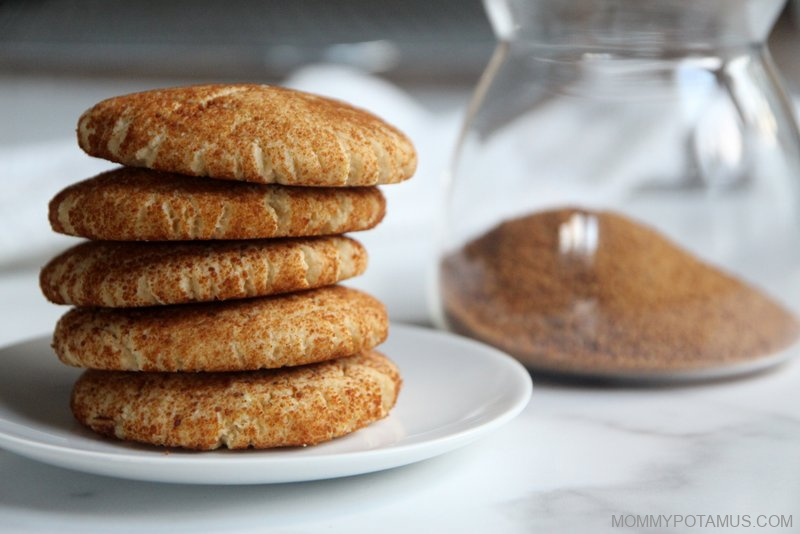 Gluten-free snickerdoodles stacked on top of each other next to a jar of cinnamon sugar