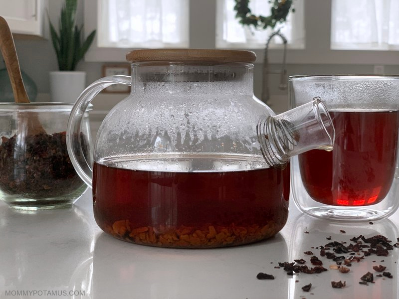 Rosehip tea in glass teapot on counter next to cup of tea and dried rosehips