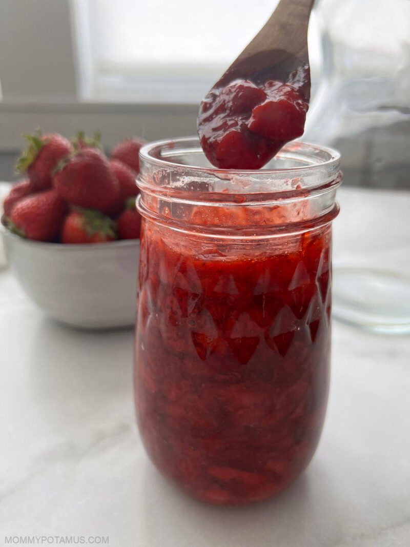 Overhead view of spoonful of strawberry sauce over a jar