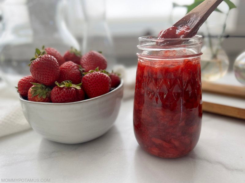 Spoon lifting strawberry sauce out of a mason jar. 