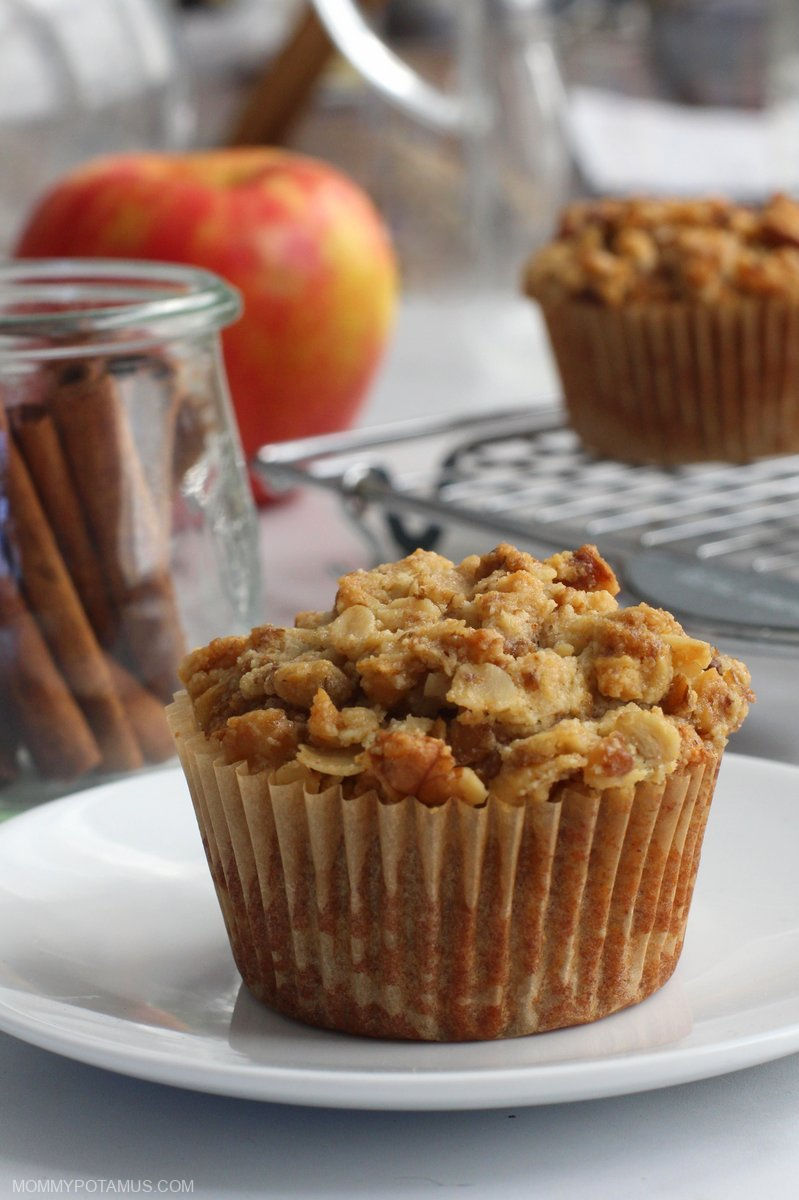 Up close view of apple cinnamon muffin on a plate with cinnamon and fresh apple in the background.