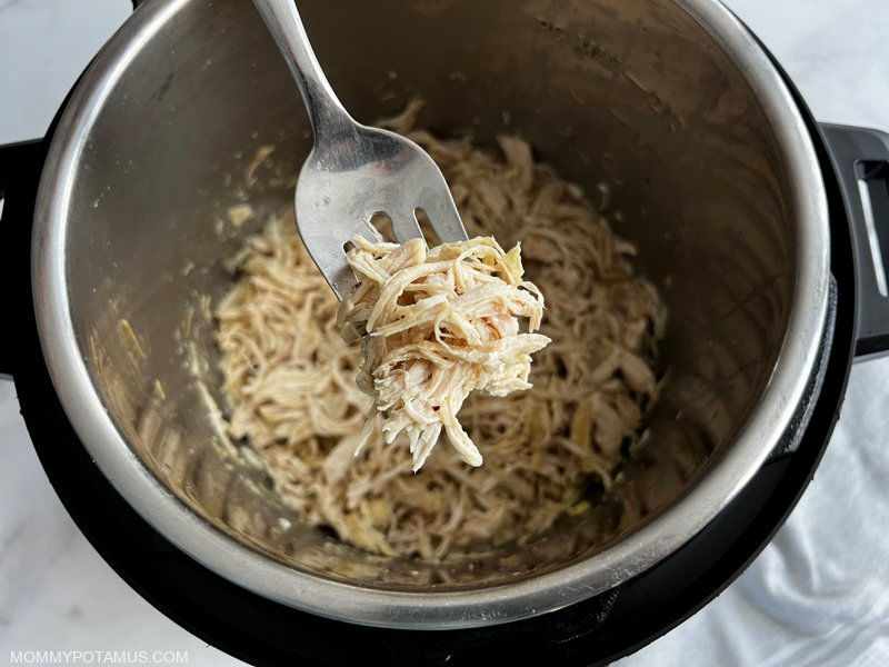 Fork full of shredded chicken lifted above Instant Pot