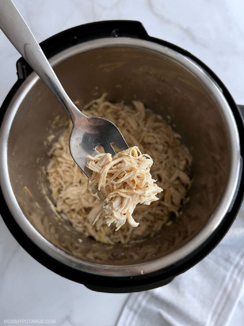 Overhead view of fork holding shredded chicken over pressure cooker