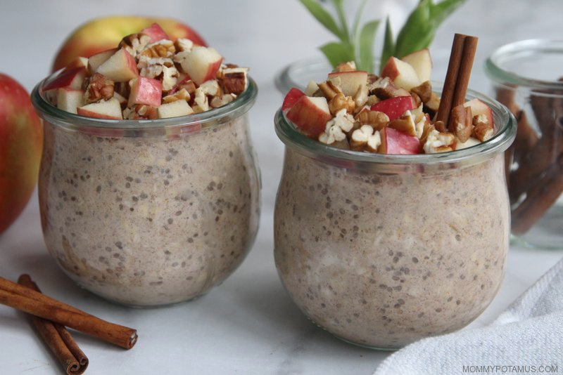 Two jars of apple cinnamon overnight oats topped with fresh diced apples and pecans on countertop