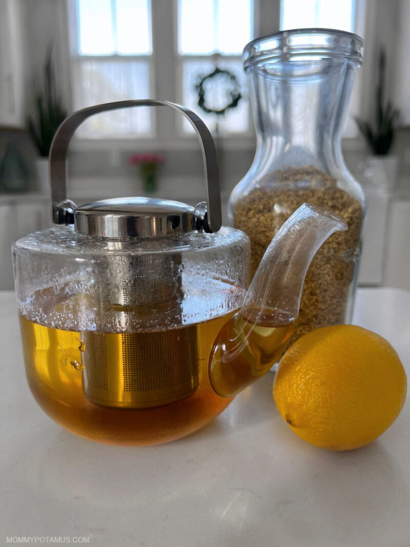 Close up of elderflower tea in glass kettle next to dried elderflowers and lemon
