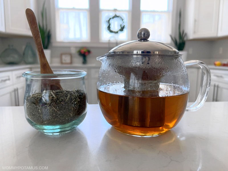 Glass kettle filled with vervain tea next to dried blue vervain on kitchen counter. 