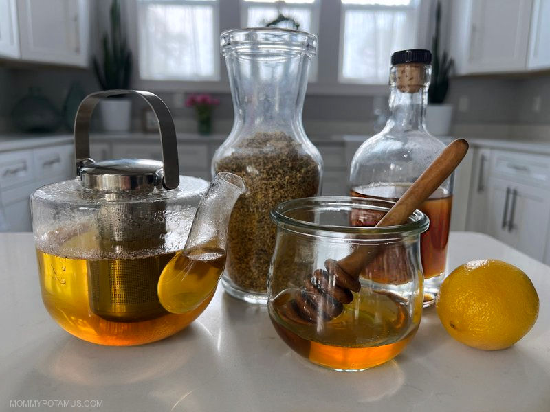 Glass teapot filled with elderflower tea, dried elderflower in jar, honey in pot, elderflower syrup