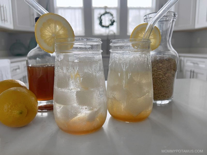 Two glasses filled with elderflower syrup, ice and sparkling water. The water and syrup are sitting in layers, unmixed. 