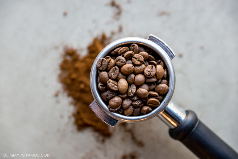 Whole coffee beans inside coffee scoop with ground coffee on countertop below