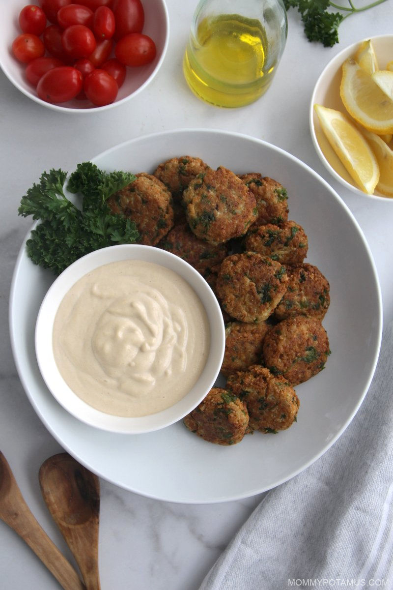 Overhead view of table setting with falafel, tahini dip, lemons, olive oil and grape tomatoes